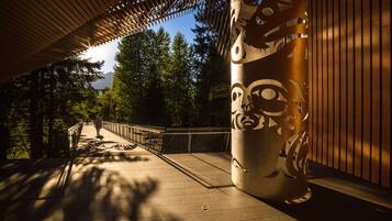 A covered walkway with a metal sculpture, a railing, and trees in the background.
