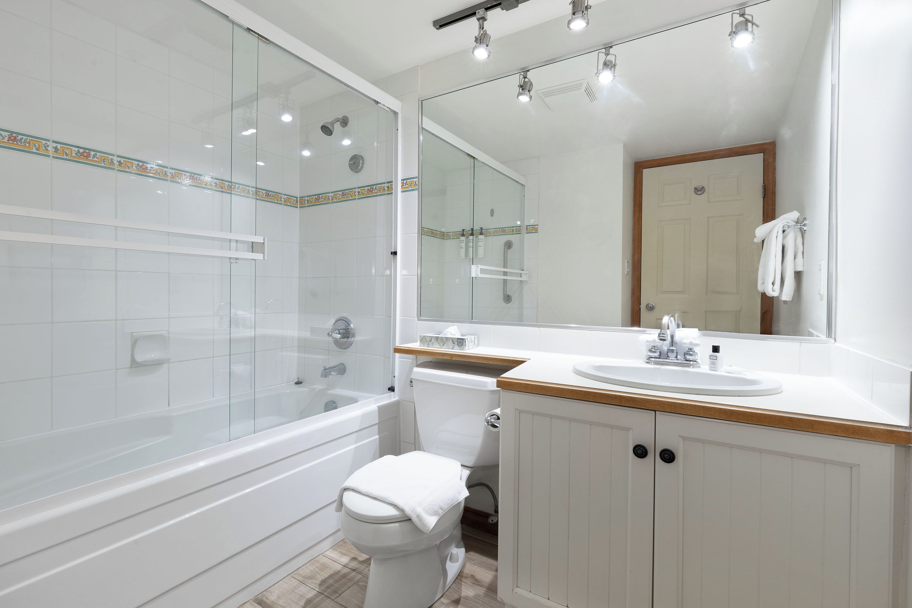 A modern bathroom with a glass-enclosed shower, a white toilet, a wooden vanity with a sink, and a large mirror.