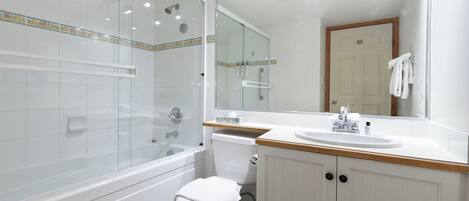 A modern bathroom with a glass-enclosed shower, a white toilet, a wooden vanity with a sink, and a large mirror.