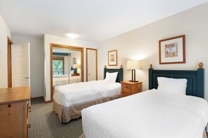 Two single beds with white linens, a dresser, and a nightstand with a lamp.