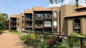 A modern multi-story building with balconies, a brick pathway, and lush greenery.