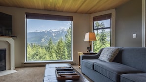 Sala de estar con un ventanal que ofrece vistas a la montaña, un sofá, una lámpara y una chimenea.