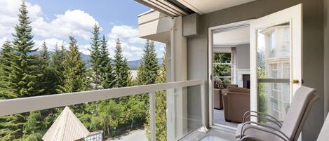 A balcony with a view of trees and mountains, a glass door, and a seating area with chairs.