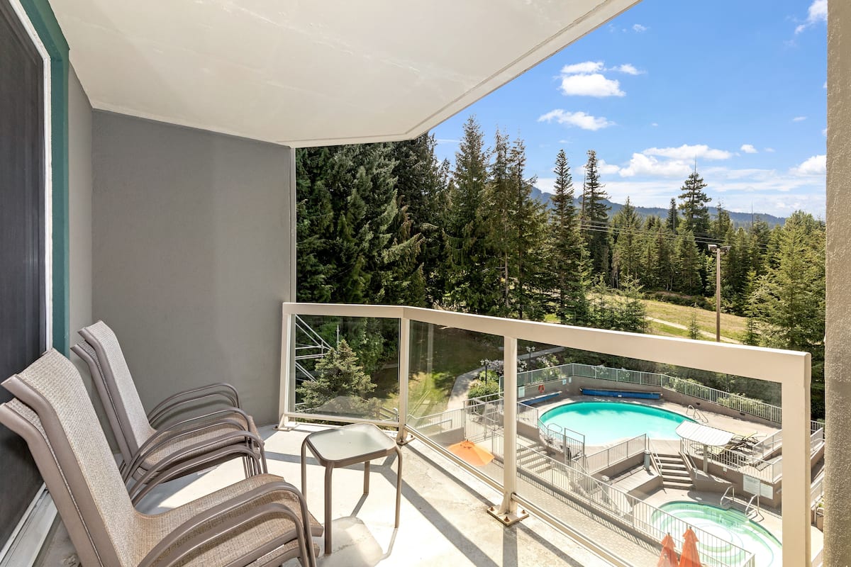Un balcon donnant sur une piscine, entourée d’arbres et de montagnes.