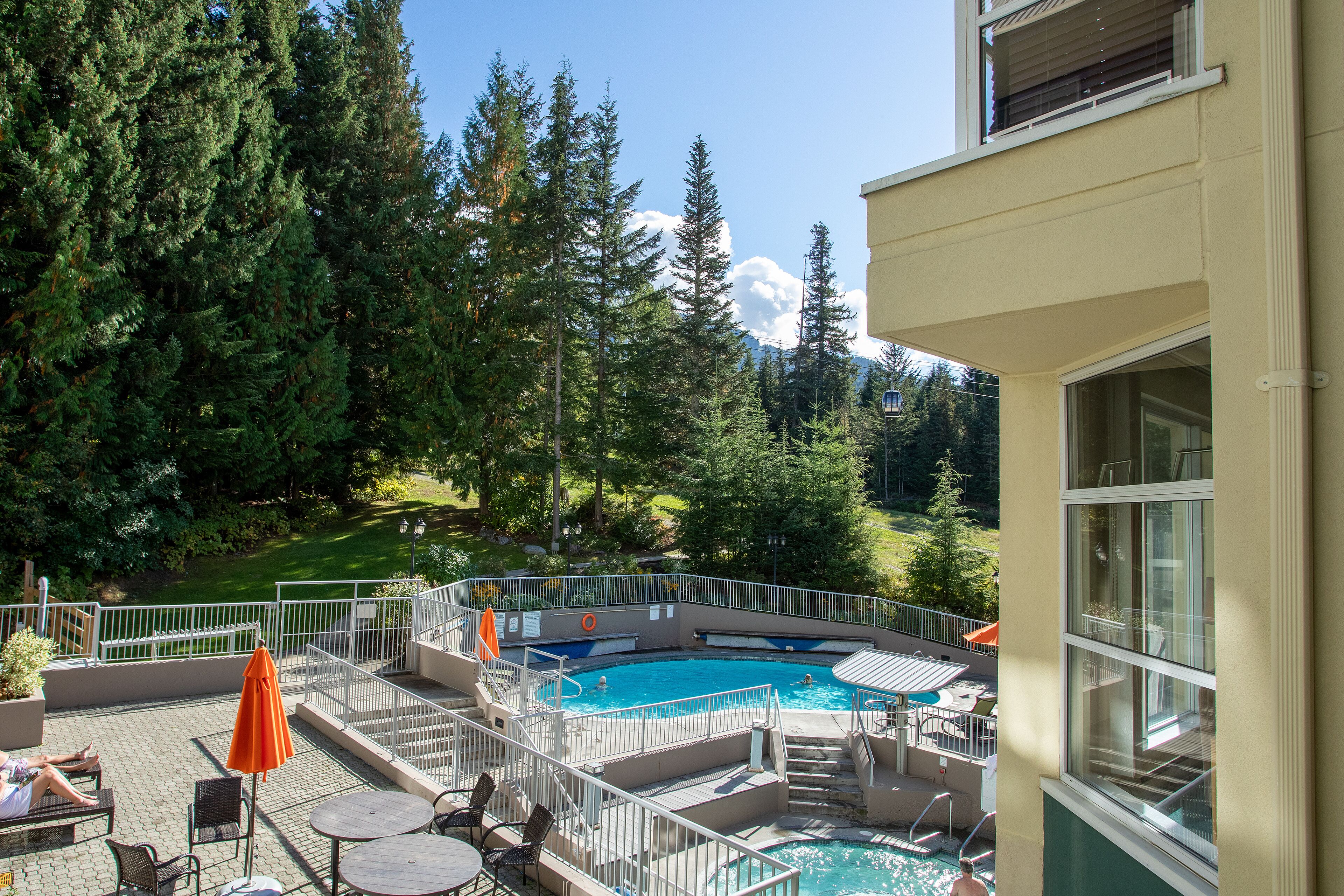A pool area with a view of trees and mountains, outdoor seating, and a building with large windows.