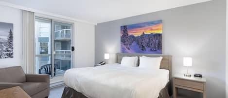 A hotel room with a large bed, a nightstand, a chair, a sofa, and a painting of a snowy landscape.