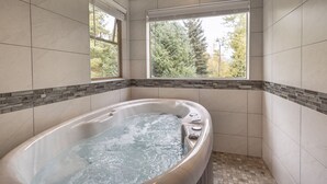 Un baño moderno con una bañera independiente, una ventana con vistas a árboles y suelo de baldosas.