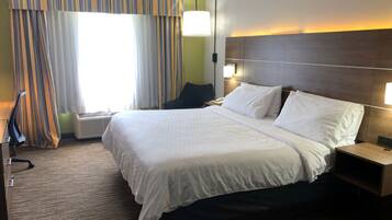 Une chambre d’hôtel avec un grand lit, une table de chevet, une lampe et une fenêtre avec des rideaux.