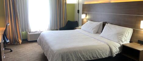 A hotel room with a large bed, a bedside table, a lamp, and a window with curtains.