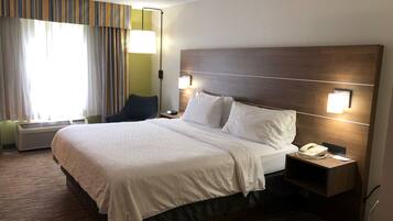Habitación de hotel con una cama grande, una mesita de noche con lámpara, teléfono y ventana con cortinas.