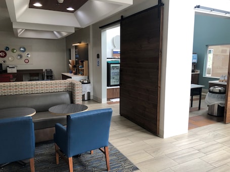 A modern interior with a seating area featuring a sofa and two chairs, a counter with a coffee machine, and a wooden partition.