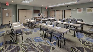 Un salón de conferencias con varias mesas y sillas, equipado con botellas de agua y papeles, en un entorno hotelero.