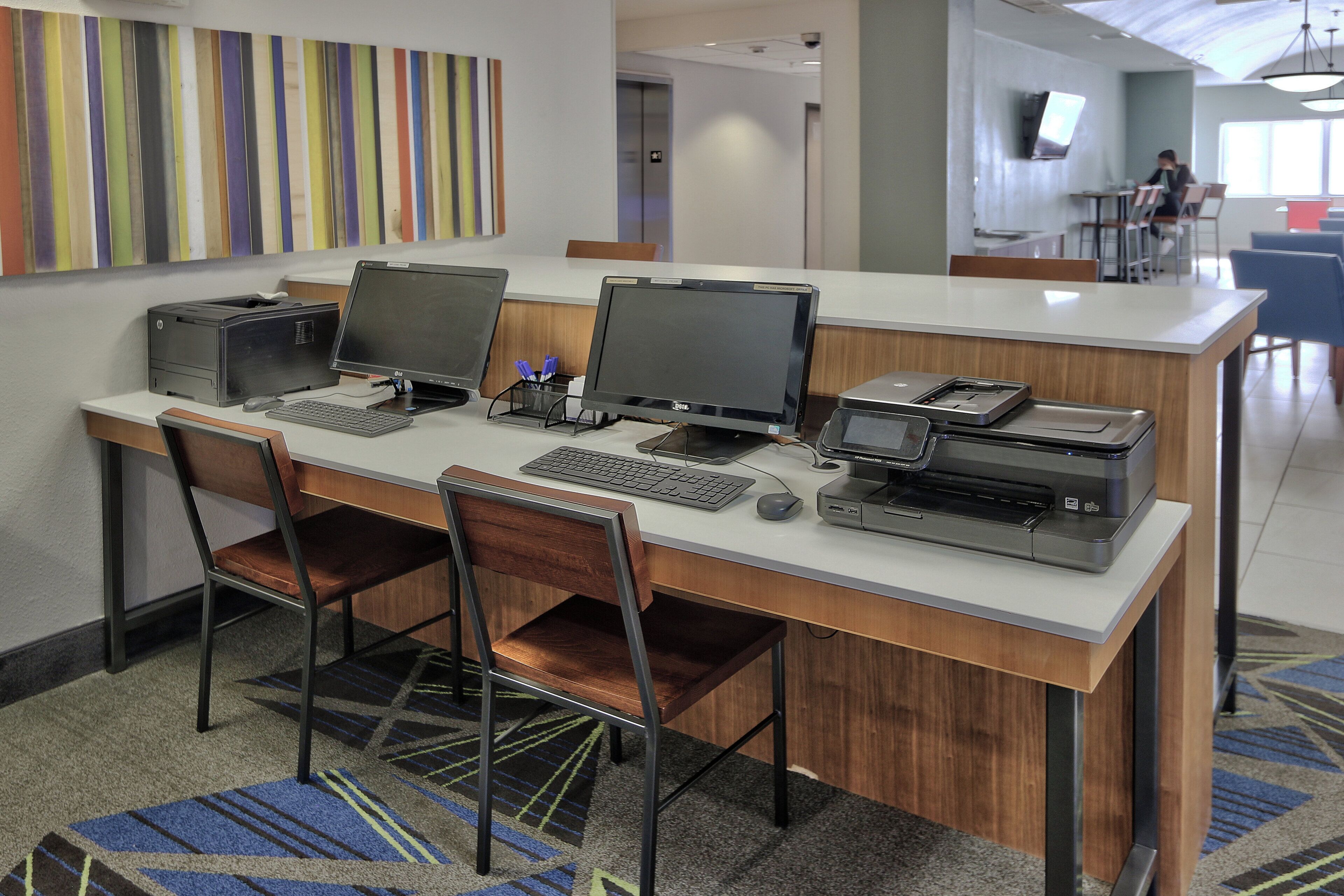 A modern office space with a long desk, multiple monitors, printers, and chairs.
