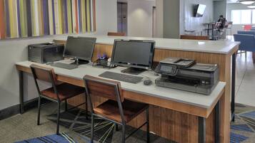 A modern office space with a long desk, multiple monitors, printers, and chairs.