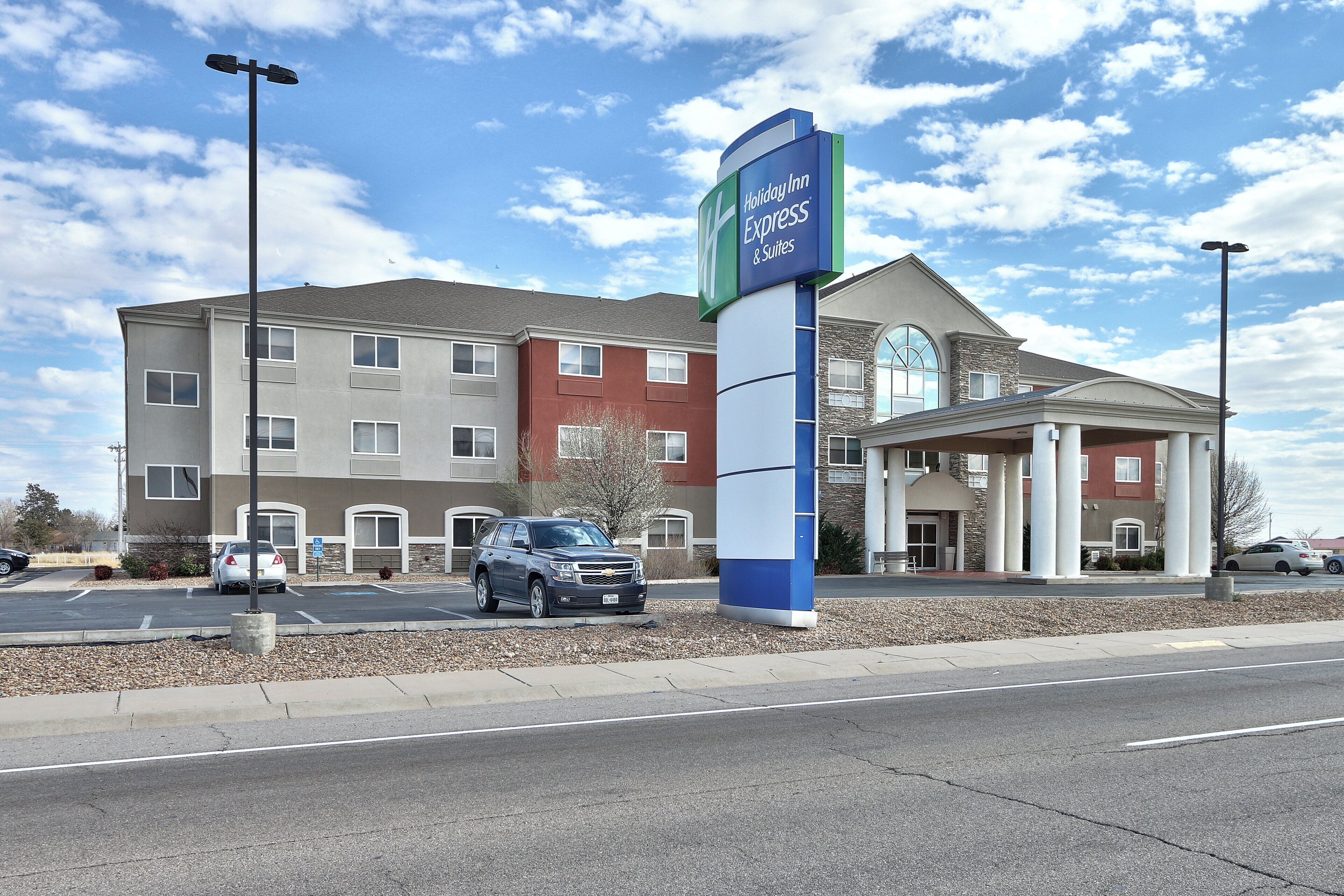 A Holiday Inn Express & Suites with a large sign, a parking lot, and a building with a mix of red and beige exterior.
