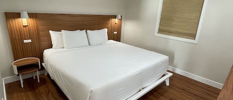 A bedroom with a wooden headboard, a bed with white linens, a nightstand, a ceiling fan, and a window with blinds.
