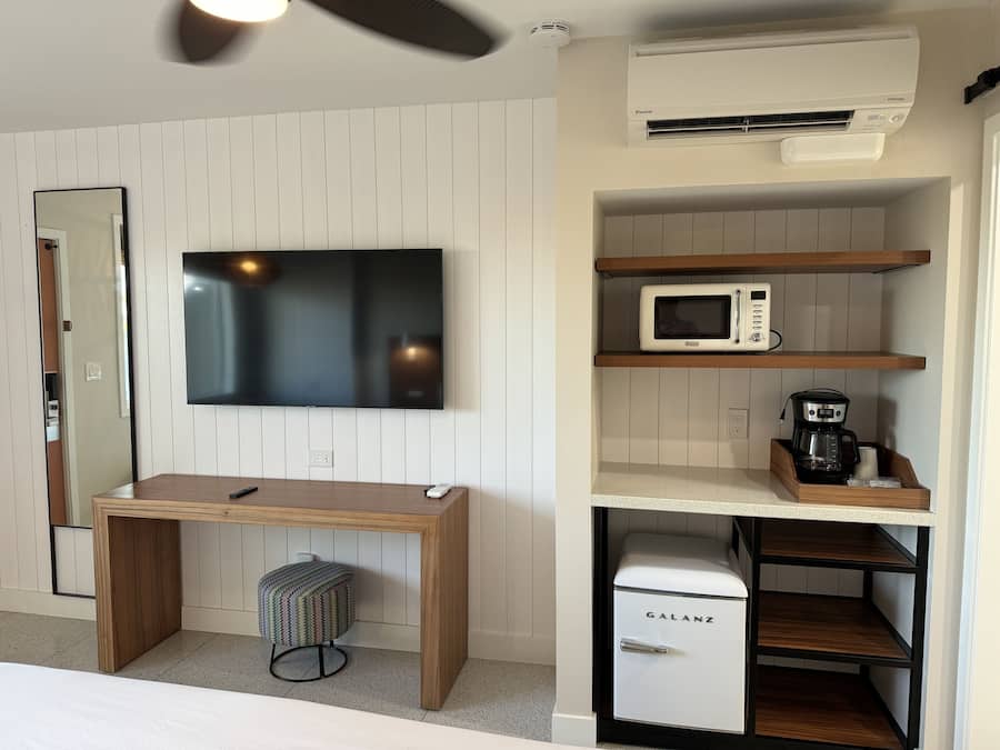 A modern kitchenette with a flat-screen TV, a microwave, a coffee maker, and a small refrigerator.