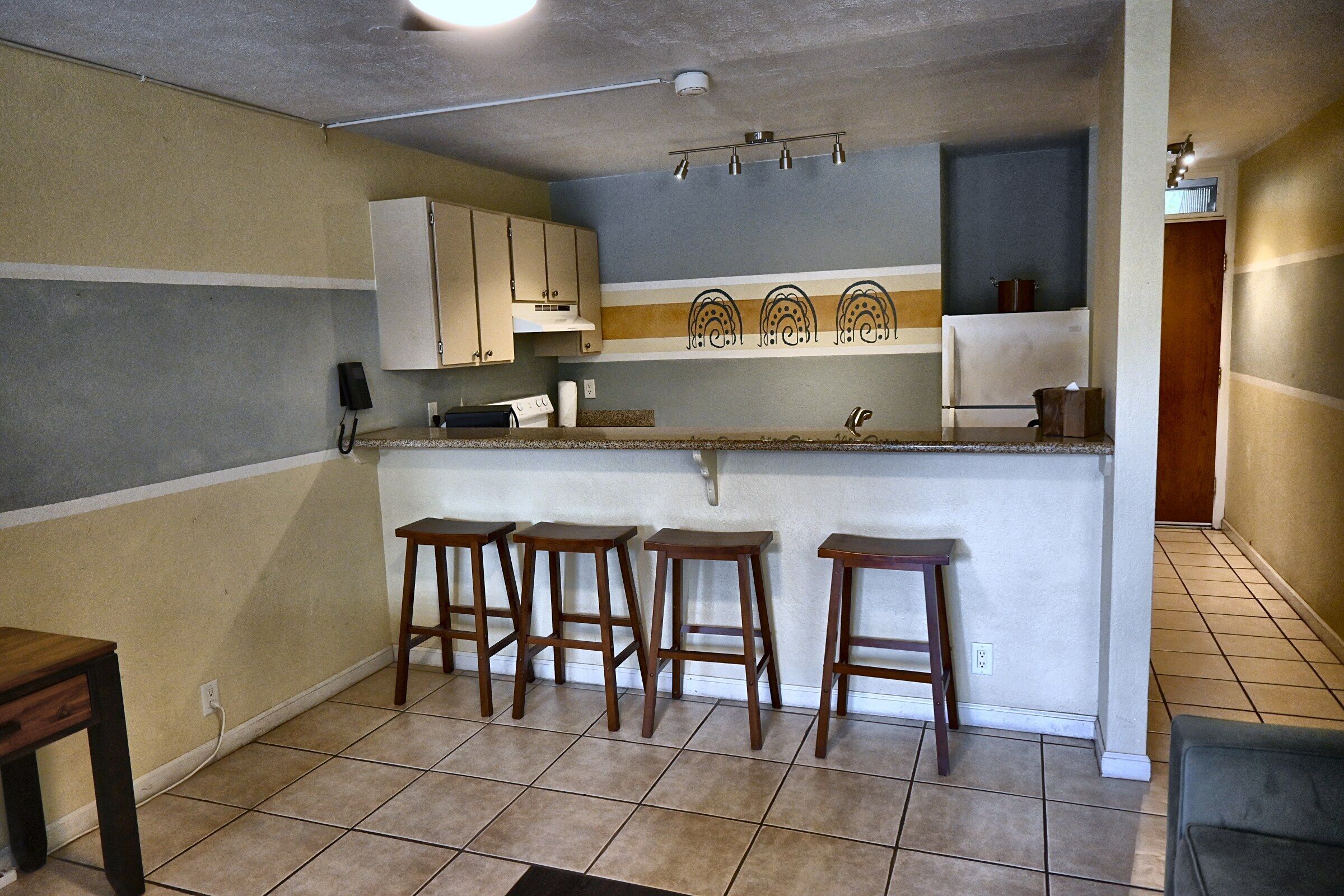 A kitchen with four wooden stools, a countertop, cabinets, and a ceiling light.