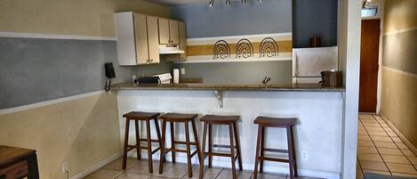 A kitchen with four wooden stools, a countertop, cabinets, and a ceiling light.