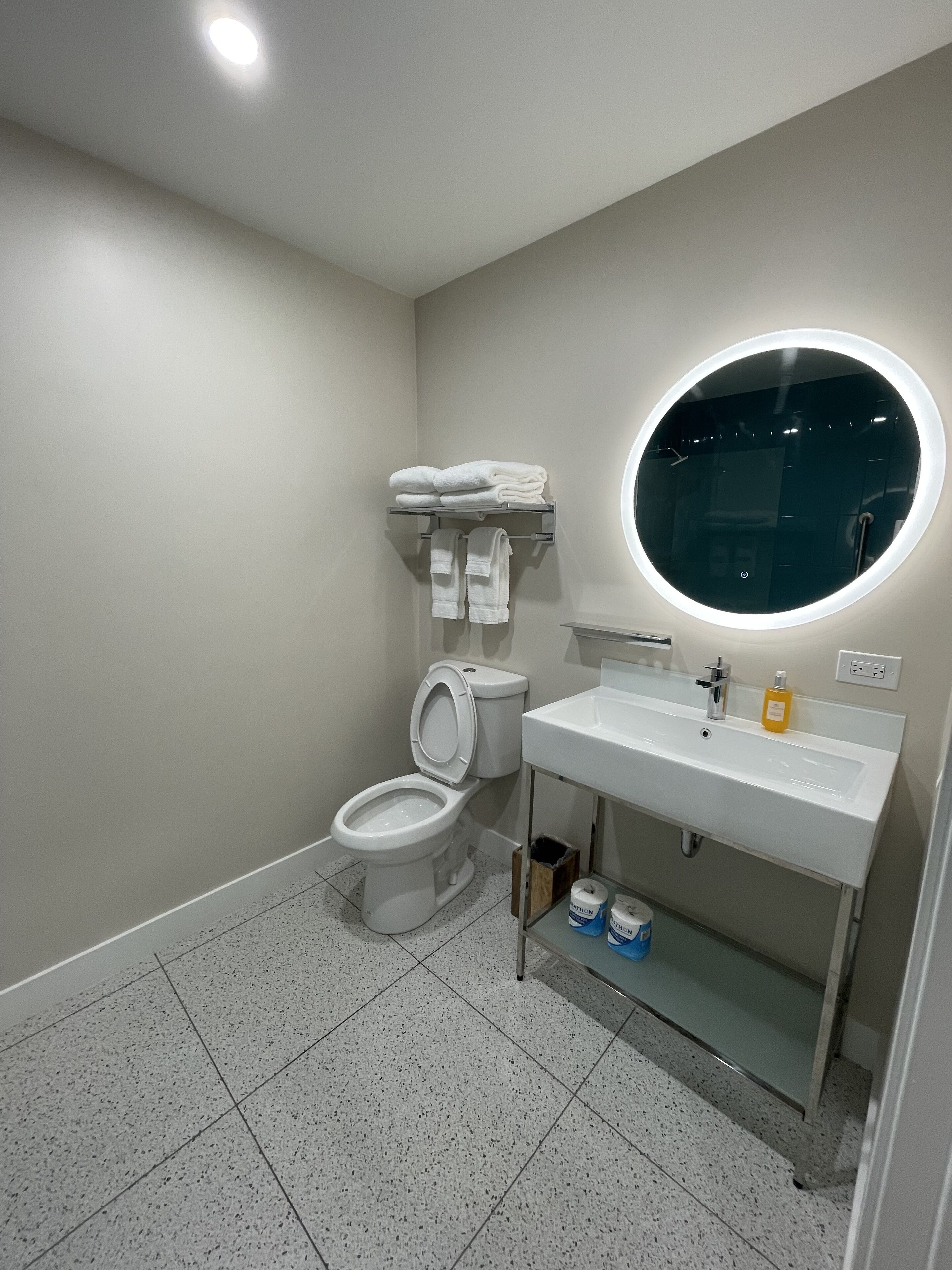 Un baño moderno con inodoro, lavamanos y un espejo redondo.