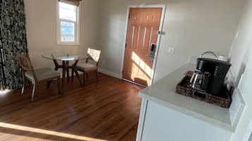 Un vaste espace de vie doté d’un plancher en bois, d’une table à manger avec des chaises, d’un luminaire suspendu et d’une porte donnant sur une autre pièce.