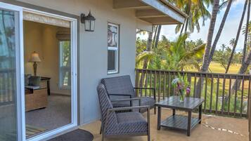 A balcony with a chair and table, a door leading to an interior room, and a view of palm trees and a golf course.