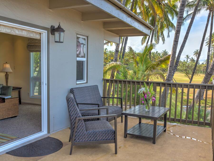 Een balkon met een stoel en tafel, een deur die naar een binnenruimte leidt, en uitzicht op palmbomen en een golfbaan.
