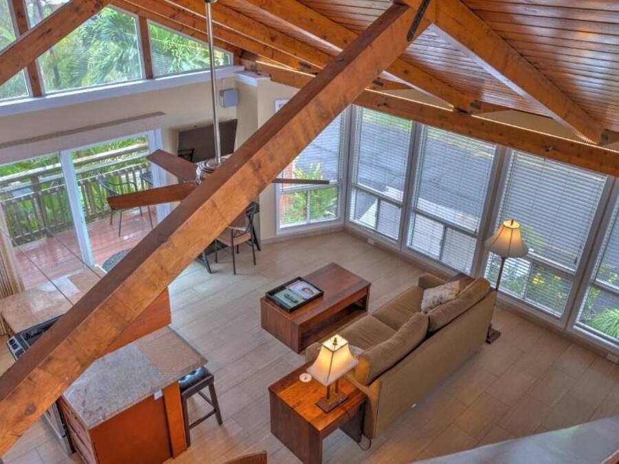 A spacious living area with a high ceiling, large windows, and a wooden staircase.