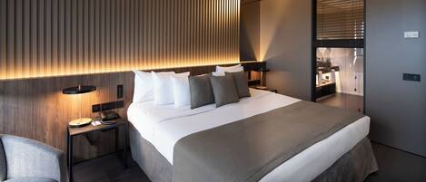 Una habitación de hotel moderna con una cama grande, una mesita de noche con lámpara y un espejo.