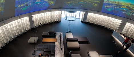 A modern conference room with a curved ceiling, large screens displaying cityscapes, and a central circular table.