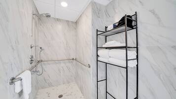 A modern bathroom with a walk-in shower, a grab bar, a towel rack, and a metal shelf with folded towels.