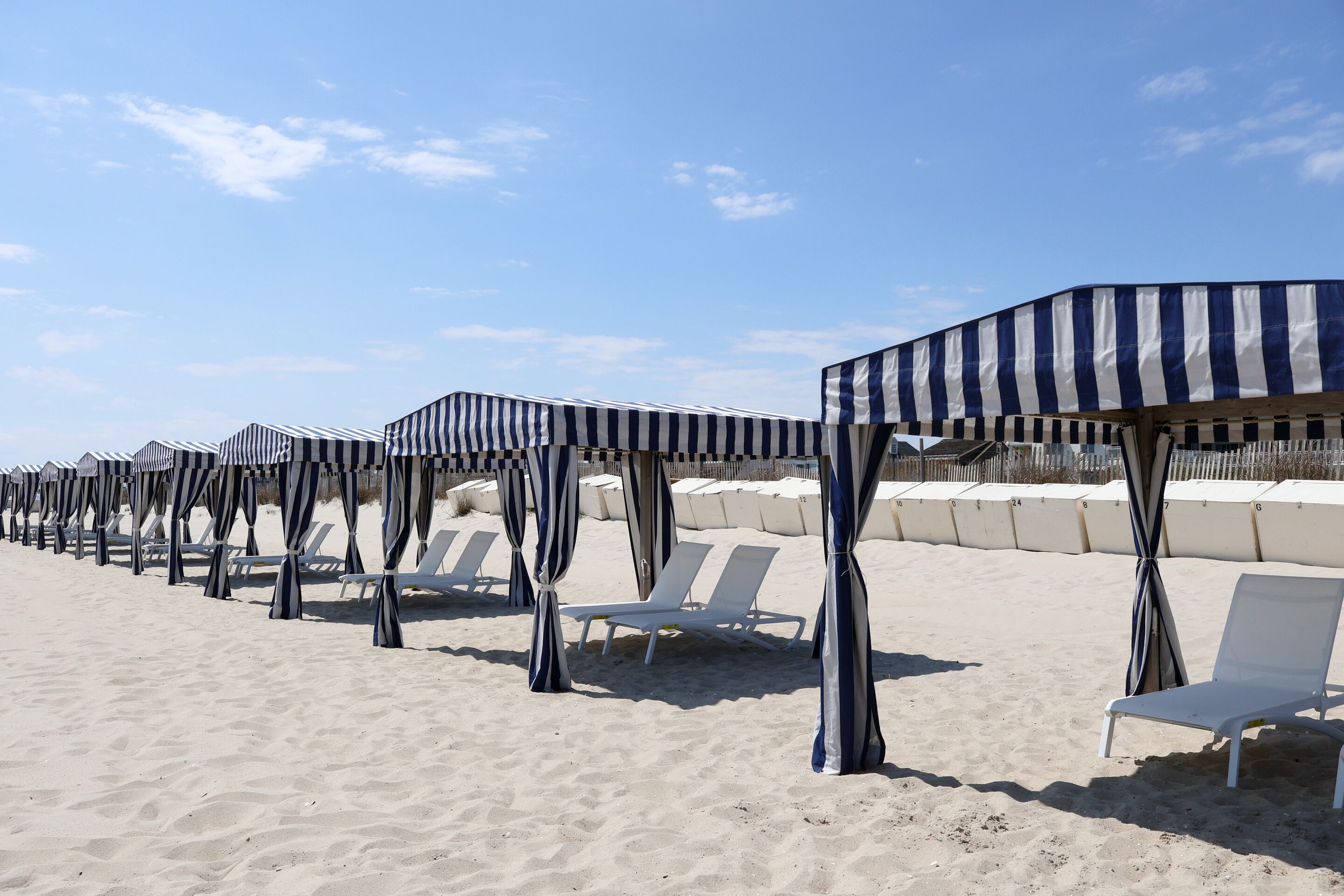 Uma praia com guarda-sóis listrados e cadeiras de praia brancas.