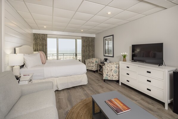 A modern hotel room with a large bed, a sofa, a TV, and a balcony with a view of the sea. - Montreal Beach Resort (Cape May)