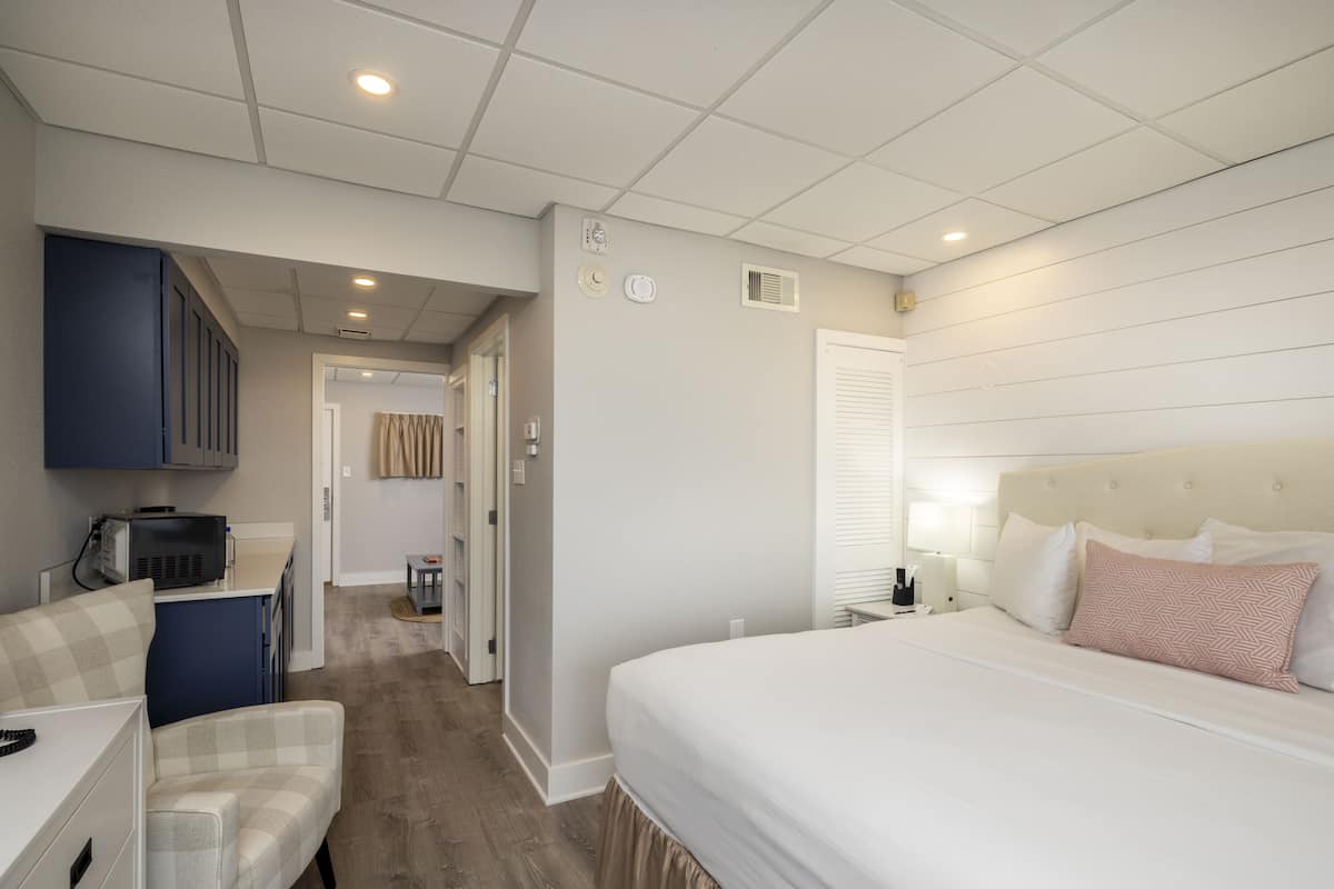 A hotel room with a bed, a desk, a chair, and a kitchenette.