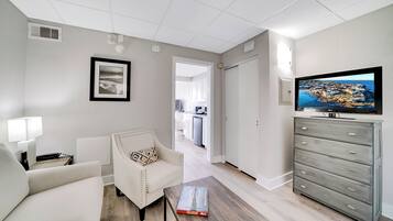 Una sala de estar moderna con un sofá, un sillón y una mesita de centro. Un televisor está montado en la pared, y hay un aparador con cajones.