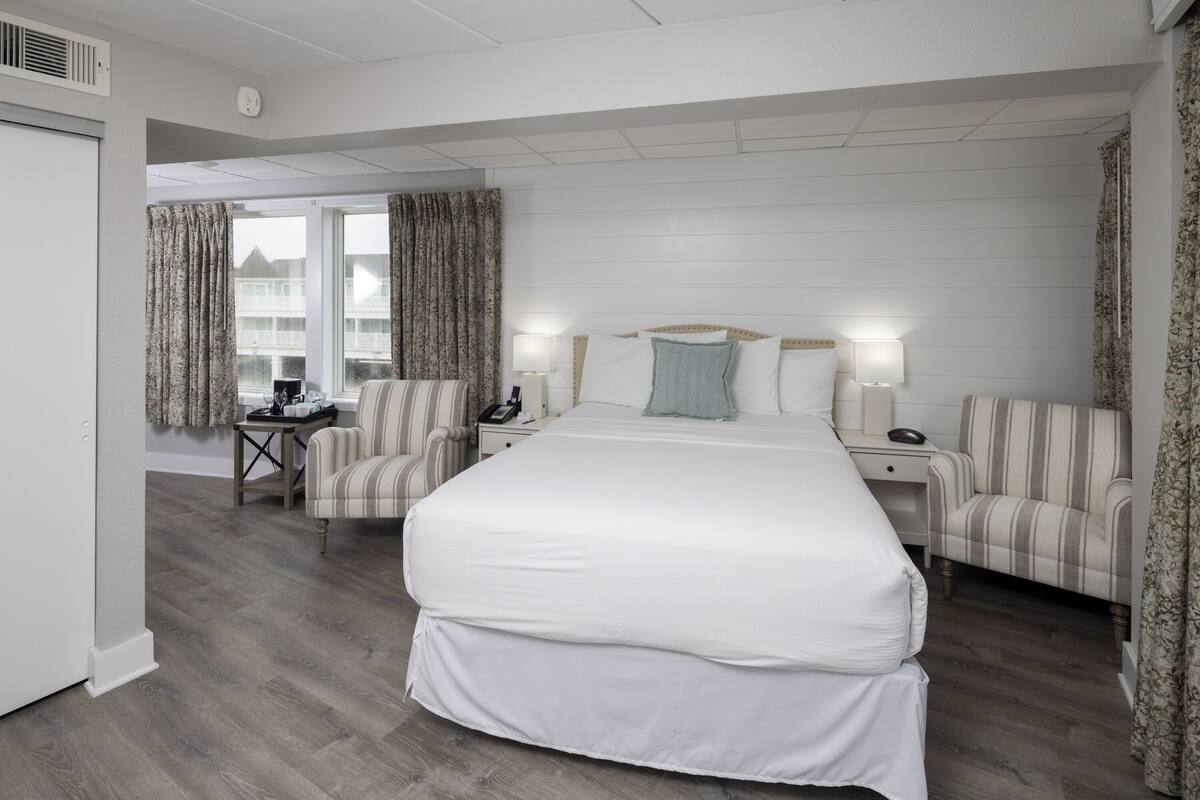 A hotel room with a large bed, two bedside tables, a chair, and a desk.