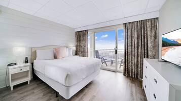 A hotel room with a large bed, a nightstand, a dresser, and a balcony with curtains.