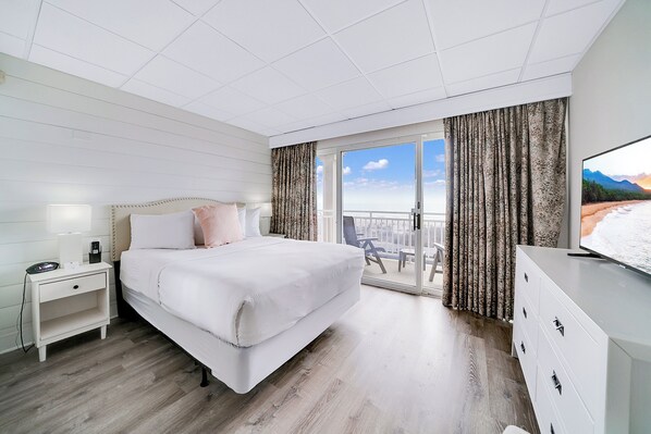 A hotel room with a large bed, a nightstand, a dresser, and a balcony with curtains. - Montreal Beach Resort (Cape May)