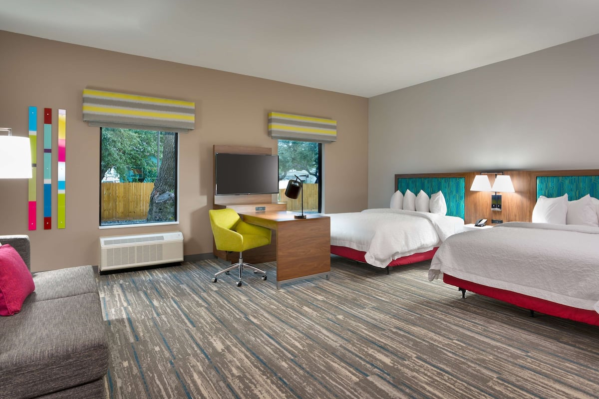 A hotel room with two beds, a desk, a chair, a TV, and a window with a view of trees.