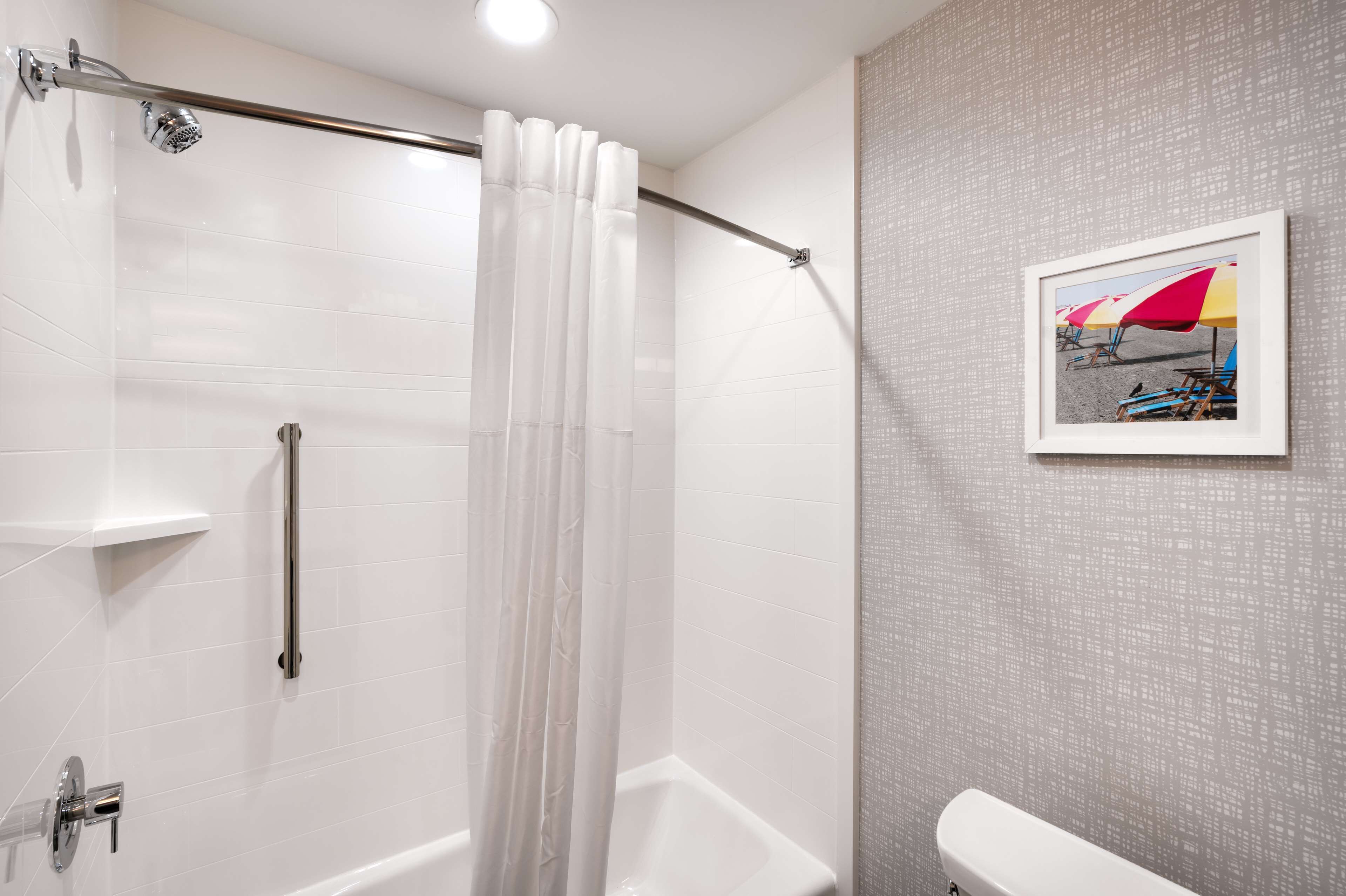 Een badkamer met een douche, toilet en een lijst met foto van strandparasols aan de muur.