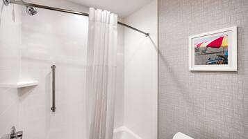 Een badkamer met een douche, toilet en een lijst met foto van strandparasols aan de muur.