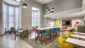 A spacious dining area with multiple tables and chairs, large windows with sheer curtains, and a flat-screen TV mounted on the wall. - Hampton Inn & Suites Rockport-Fulton (Fulton)