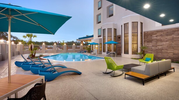 A modern outdoor pool area with lounge chairs and umbrellas, a pool, and a building with a 'Welcome' sign. - Hampton Inn & Suites Rockport-Fulton (Fulton)