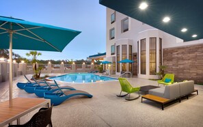 A modern outdoor pool area with lounge chairs and umbrellas, a pool, and a building with a 'Welcome' sign. - Hampton Inn & Suites Rockport-Fulton (Fulton)