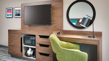 Habitación de hotel con escritorio de madera, televisión de pantalla plana, espejo redondo y silla verde.