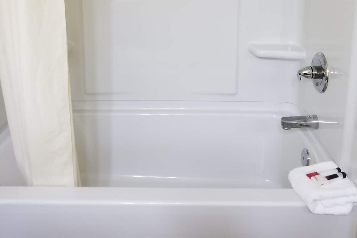 Una bañera blanca con cortina de ducha, una toalla y una botella de champú.