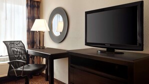 A hotel room with a television, a desk, a chair, a lamp, and a window with curtains.