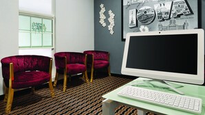 A room with a large window, a framed picture of Iowa, three red velvet chairs, a white desk with a keyboard, and a patterned carpet.