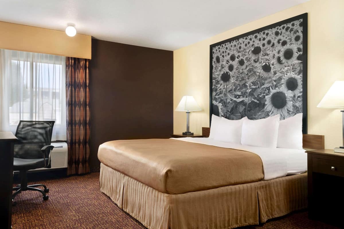 Habitación de hotel con una cama grande, dos lámparas de noche, un escritorio con silla, una obra de arte floral grande en la pared y una ventana con cortinas.
