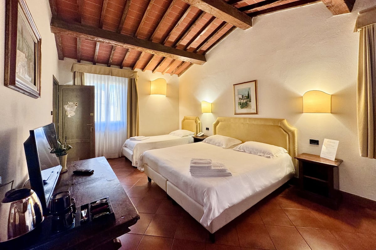 A hotel room with two beds, a desk with a kettle, a wardrobe, and a painting on the wall.